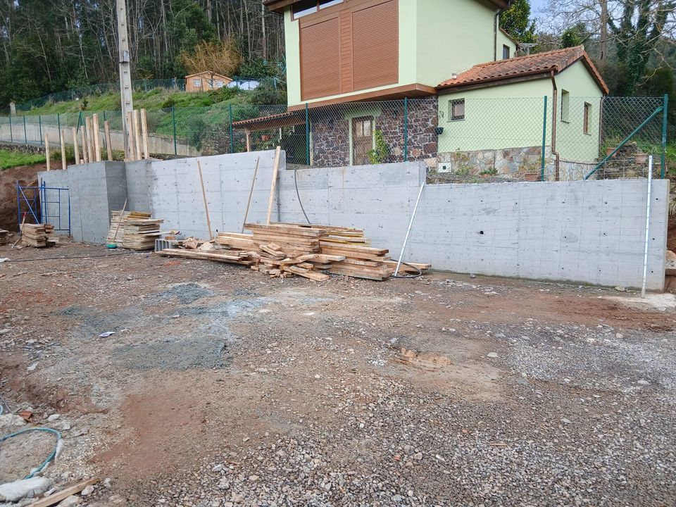 Muro de contención perimetral de la parcela, con acopio de madera de encofrado.