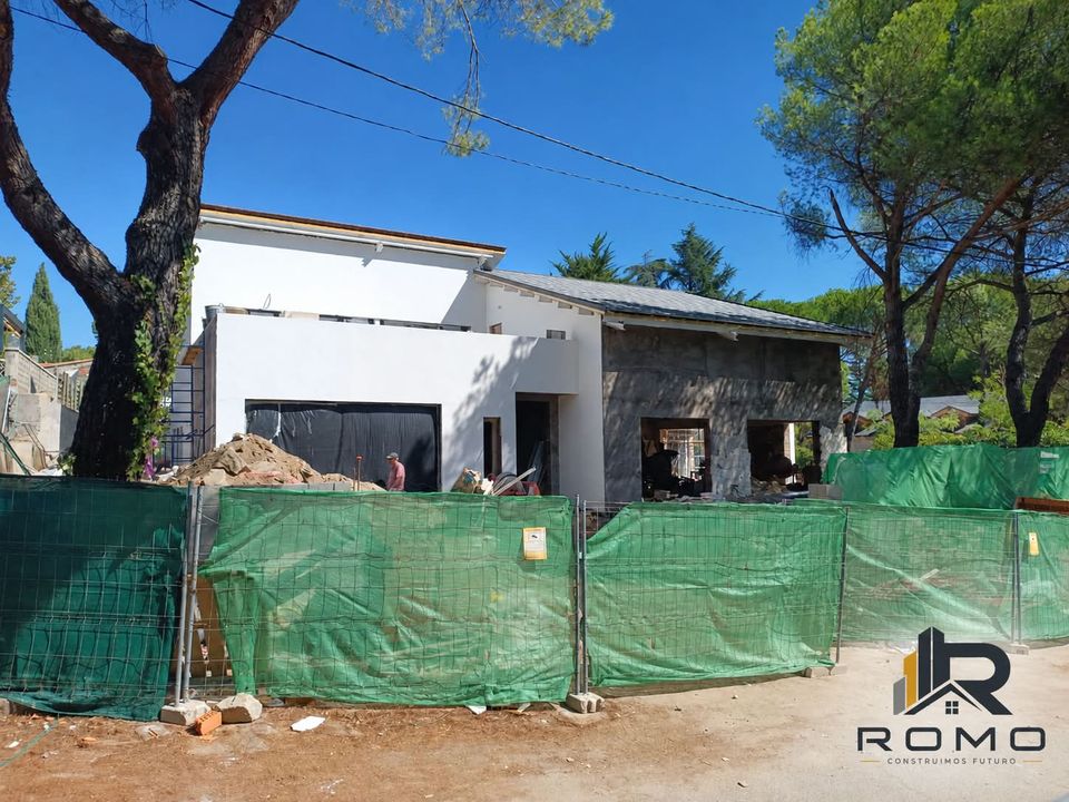 Chalet contemporáneo en obra en la Sierra de Madrid: volúmenes blancos de líneas rectas en una parcela entre pinos.