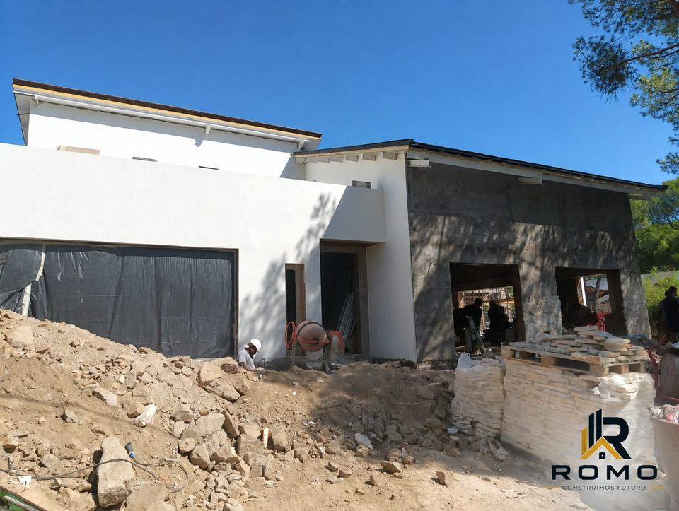 Fachada principal y volumen del garaje del chalet contemporáneo de la Sierra, con la parcela aún en movimiento de tierras.